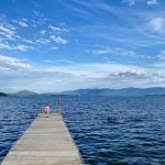 Girl in pink dress stands at the end of a dock on Lake Pend Oreille, Idaho, as part of an epic family road trip on the International Selkirk Loop.