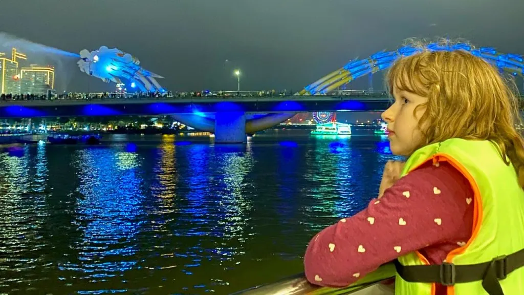 Aster stands at the rail of a tour boat and watches the dragon bridge in Da Nang, Vietnam