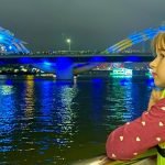 Aster stands at the rail of a tour boat and watches the dragon bridge in Da Nang, Vietnam