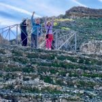 Kids with dad wave from atop the Roman amphitheater in Italica, Spain.