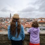 Two kids look out over a hilltop wall at the skyline of Porto, Portugal