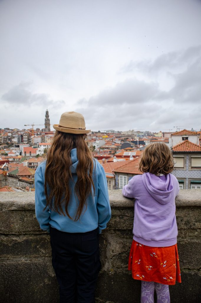 Two kids look out over a hilltop wall at the skyline of Porto, Portugal