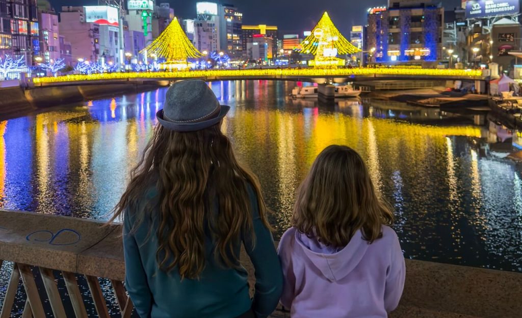 Two kids look out at a nighttime scene of the river and lights in Fukuoka, Japan