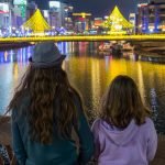 Two kids look out at a nighttime scene of the river and lights in Fukuoka, Japan